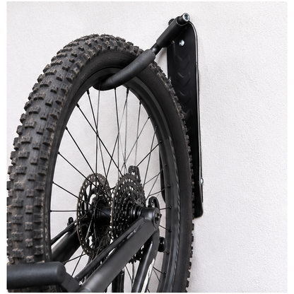 Detalle del colgador negro instalado en pared sujetando una rueda de bicicleta